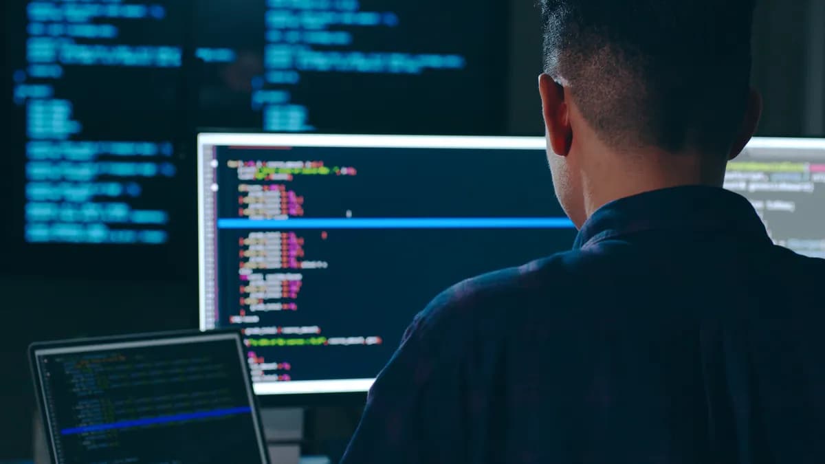 A software developer writes code while using an external monitor in an office setting